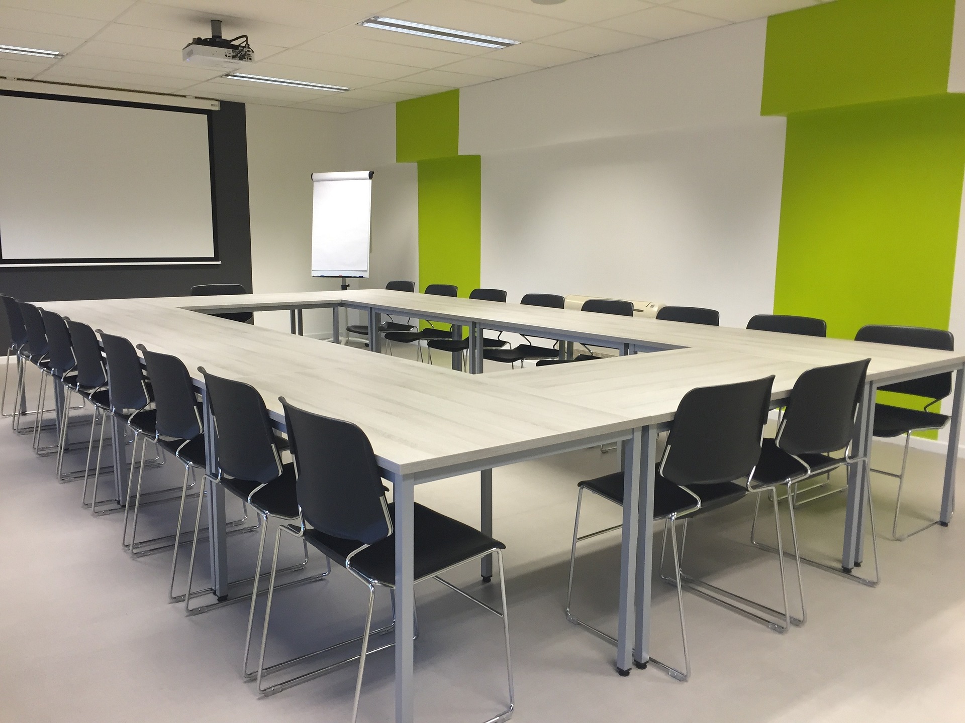 photograph of conference room with tables and chairs in a rectangle and a presentation screen at one side